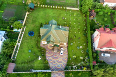 Aerial top view of house shingle roof and a car on paved yard with green grass lawn.