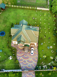 Aerial top view of house shingle roof and a car on paved yard with green grass lawn.
