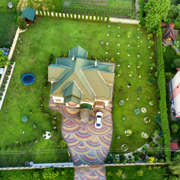 Aerial top view of house shingle roof and a car on paved yard with green grass lawn.